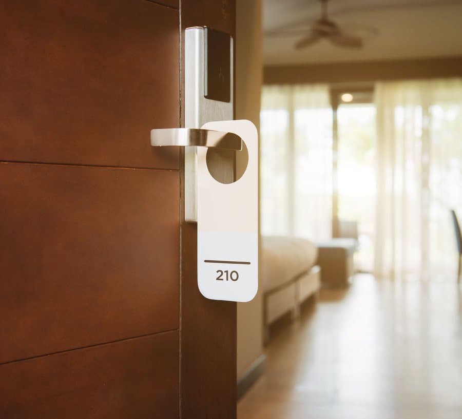 An open hotel room door with a room 210 tag on the handle and a sunlit room beyond.