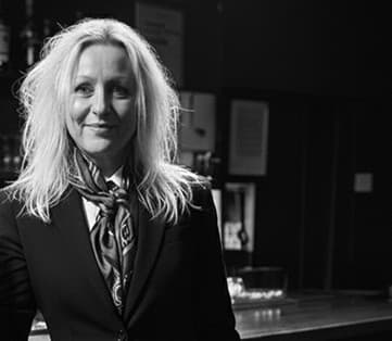 Black and white portrait of Kim Lehult, TripQuest advisor, in a tailored jacket and patterned scarf.